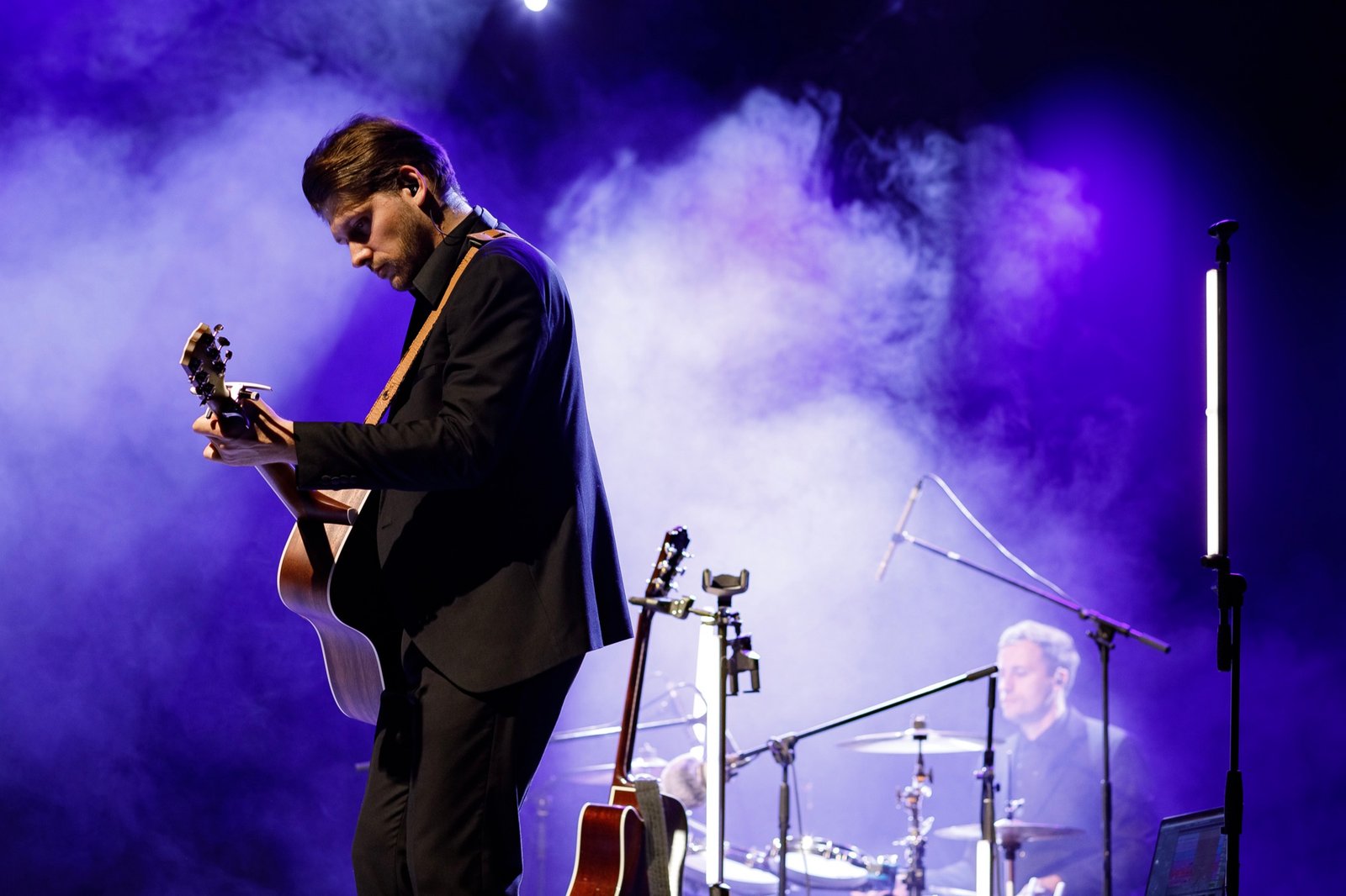 Justinas Stanislovaitis with a guitar on a smoke-filled stage in blue light
