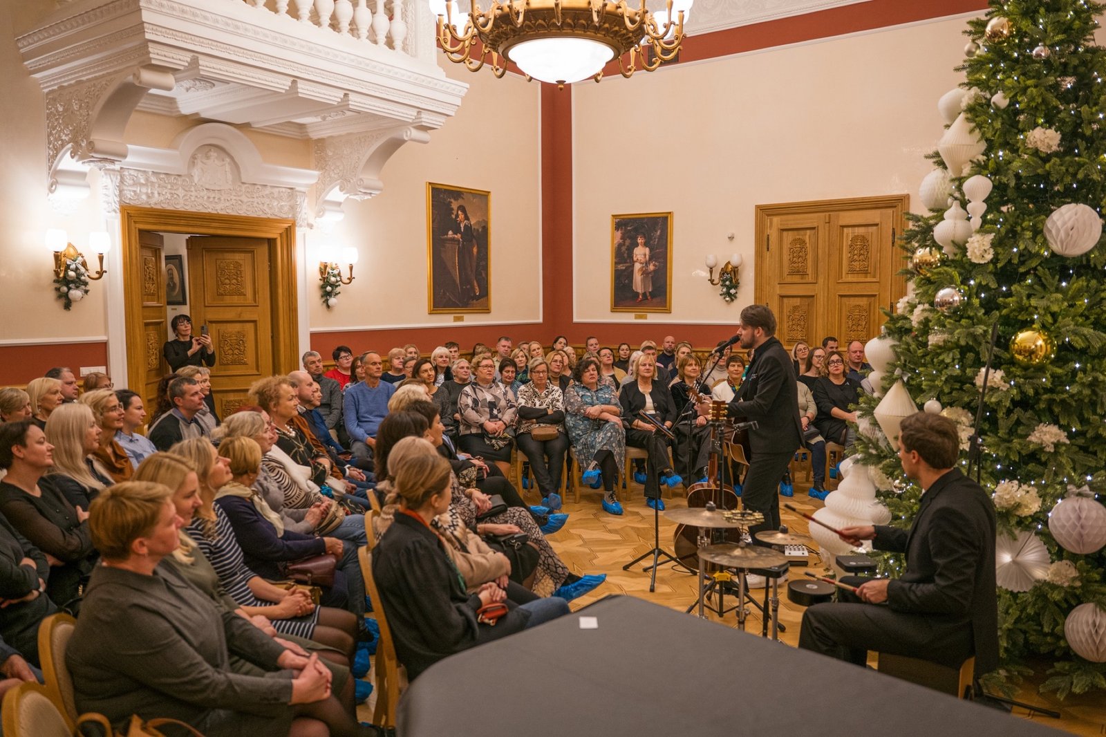 A concert in a full manor hall with a Christmas tree